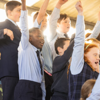 children raising arms in the air performing as part of the Junior School Choir